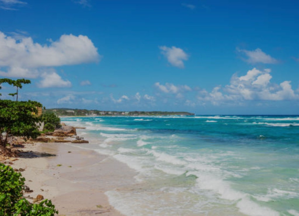 Turquoise waves rolling onto a white sand Jamaica beach with lush tropical coastline near Falmouth for cruise passenger beach excursions